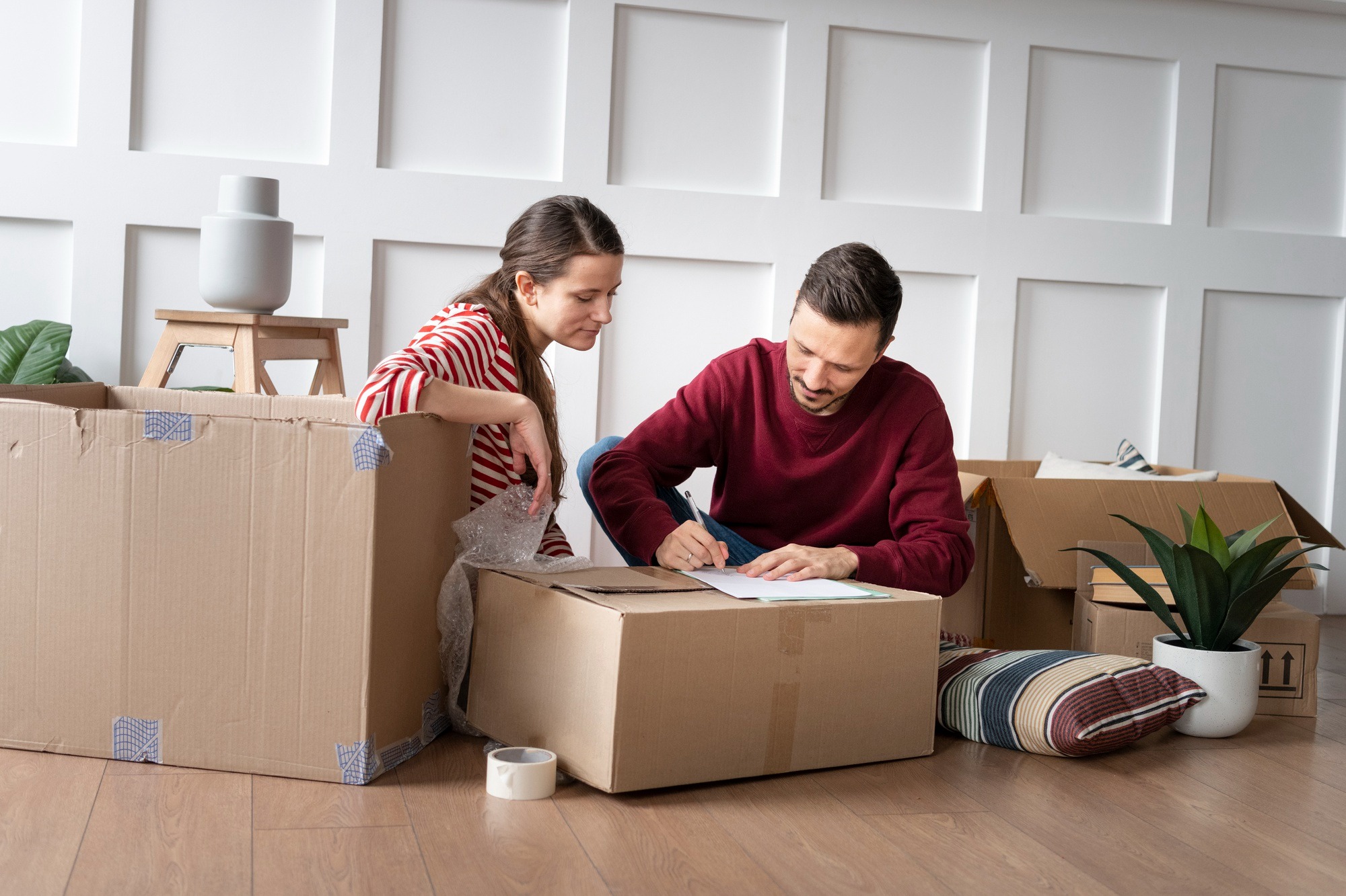 Ein Mann und eine Frau sitzen zuhause und packen Kartons für den Umzug. Umzugsunternehmen in der Nähe Berlin Hering.