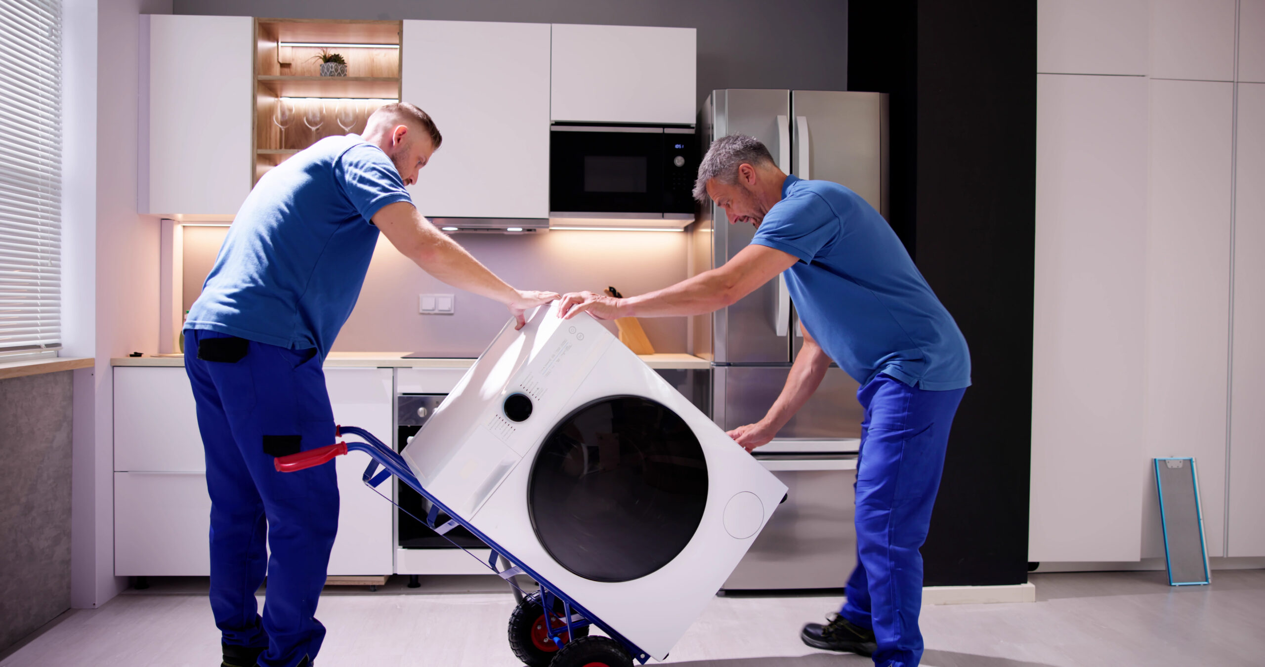 Zwei Umzugshelfer in blauer Kleidung tragen eine Waschmaschine. Umzugsunternehmen Kosten Berlin Hering.